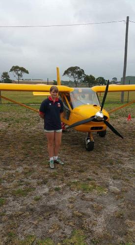A young female standing in front of a yellow light aircraft